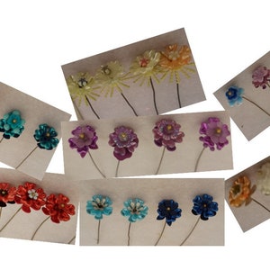 May include: Assortment of colorful flower pins with glitter accents. The pins are arranged in rows on a white background. The flowers are made of various materials, including fabric, plastic, and metal.