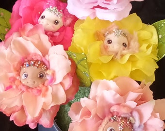 May include: A whimsical floral arrangement featuring fabric flowers in shades of pink, peach, and yellow. Each flower has a doll face at its center, adorned with decorative accents. Green leaves add a touch of contrast to the colorful display.
