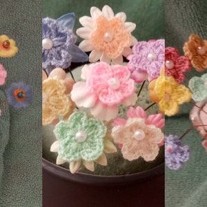May include: A bouquet of crocheted flowers in various pastel colors, including pink, blue, yellow, and green, with pearl accents. The flowers are arranged in a ceramic vase with a textured surface.