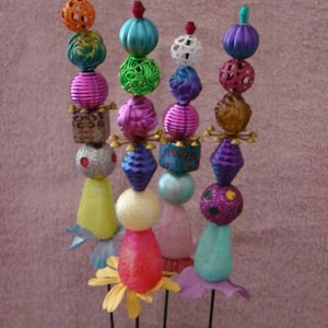May include: Four colorful beaded flower stems with a variety of textures and patterns. Each stem has a different color scheme and features a variety of beads, including round, square, and cylindrical shapes. The stems are arranged in a pot with green moss.