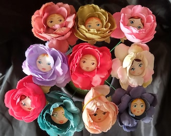 May include: A collection of handmade flower dolls with painted faces. The dolls are made of fabric and have colorful petals in shades of pink, red, purple, yellow, and blue. Each doll has a unique expression.