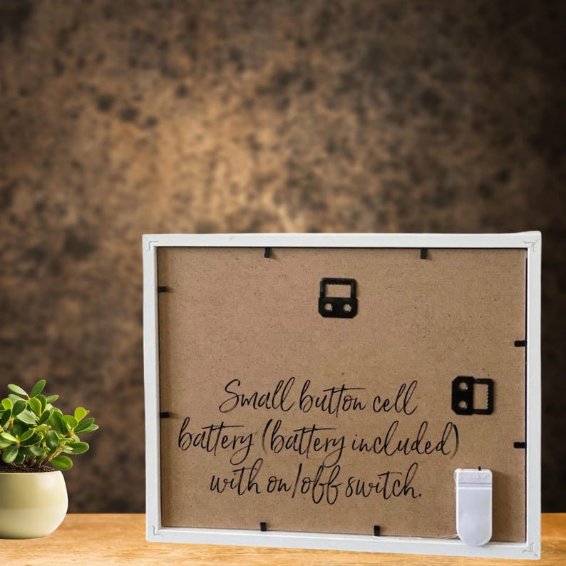 May include: White picture frame with a brown cardboard backing. The back of the frame has text that reads "Small button cell battery (battery included) with on/off switch."