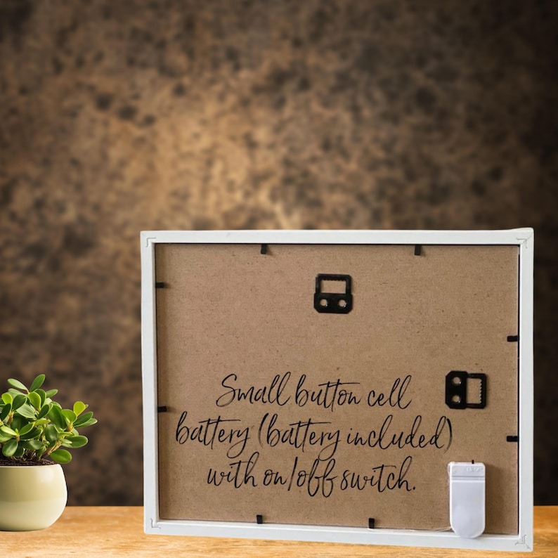 May include: White picture frame with a brown cardboard backing. The back of the frame has a small button cell battery (battery included) with an on/off switch.