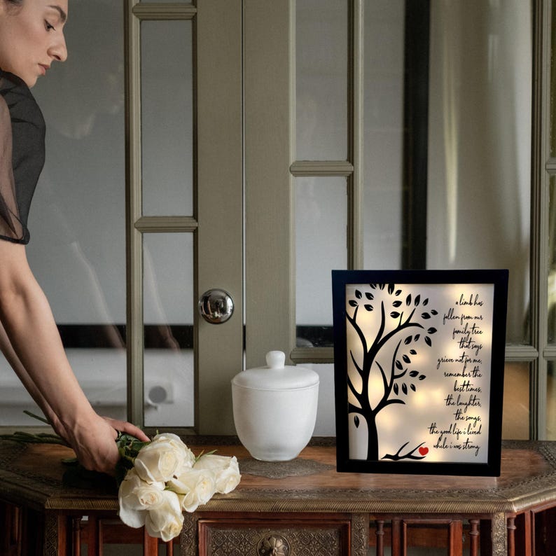 May include: A black framed illuminated wall art with a silhouette of a tree and a red heart. The text reads "A link to pollen from our family tree that sings grieve not for me remember the best times the laughter the songs the good life I lived while I was strong."