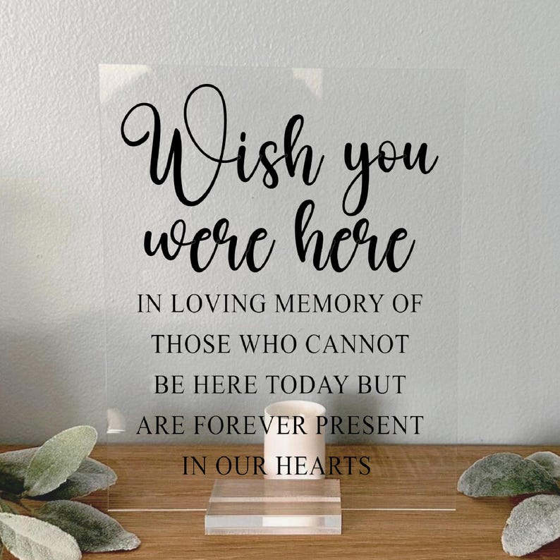 May include: A clear acrylic sign with the text "Wish you were here" in black cursive font. The sign also includes the text "In loving memory of those who cannot be here today but are forever present in our hearts."