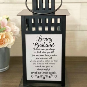 May include: Black metal lantern with a white insert featuring a poem about a loving husband. The poem reads: "Loving Husband I think about you always, I think about you still, You have never been forgotten, and you never will. I hold you close within my heart and there you will remain, to walk and guide me through my life, until we meet again."