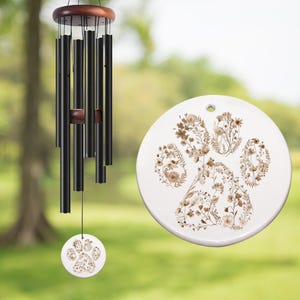 May include: Black wind chimes with a wooden top and a paw print design. The wind chime has black tubes and a round, white paw print pendant with a floral design. A matching paw print decor is also visible.