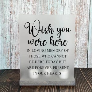 May include: A white sign with black text that reads "Wish you were here. In loving memory of those who cannot be here today but are forever present in our hearts."