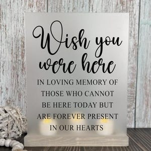 May include: A white sign with black text that reads "Wish you were here. In loving memory of those who cannot be here today but are forever present in our hearts."