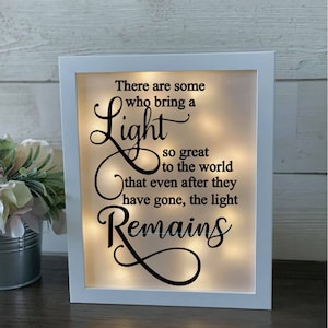 May include: White framed light-up sign with the text "There are some who bring a Light so great to the world that even after they have gone, the light Remains".
