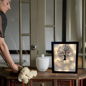 May include: A black framed light-up sign with a silhouette of a tree with red birds and the text "A limb has fallen, we're together again".