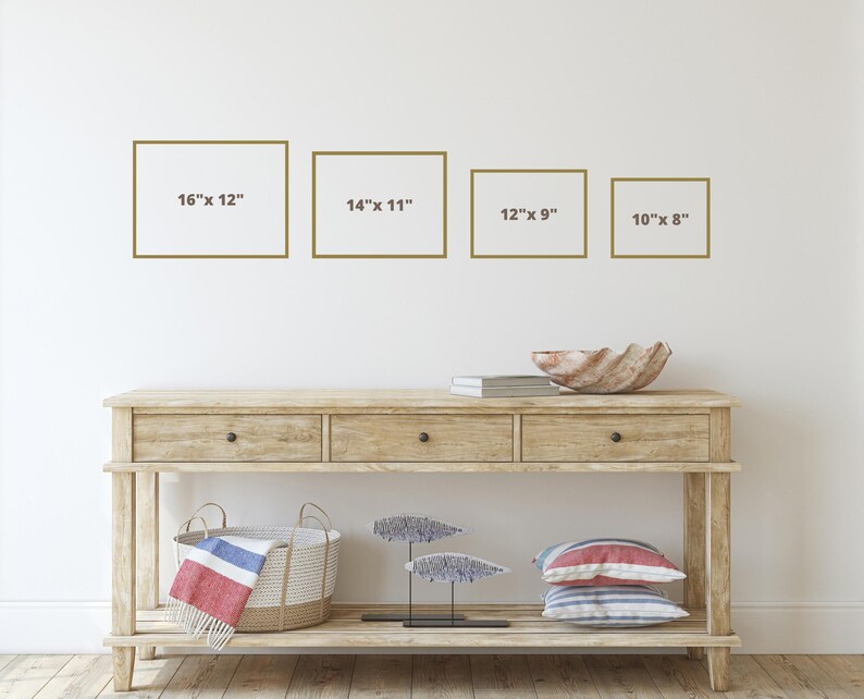 Op de afbeelding: Vier ingelijste foto's aan een witte muur, met de afmetingen van elke foto eronder. De foto's zijn 16 inch bij 12 inch, 14 inch bij 11 inch, 12 inch bij 9 inch en 10 inch bij 8 inch. Voor de muur staat een houten consoletafel met twee laden en een onderplank. Op de tafel staan een schelpenkom, een stapel boeken, een geweven mand en een decoratief metalen beeld.