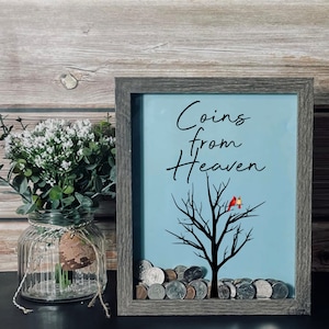 May include: A gray wooden shadow box with a blue background and the text "Coins from Heaven" in black script. A black silhouette of a tree with two red cardinals perched on a branch. The box is filled with coins.