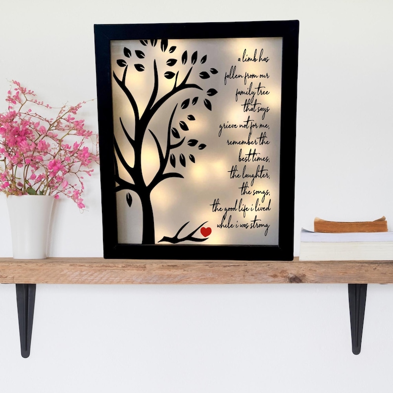 May include: A black framed illuminated wall art piece with a silhouette of a tree and a red heart on a branch. The text reads "A limb has fallen from our family tree that says grieve not for me, remember the best times, the laughter, the songs, the good life I lived while I was strong."