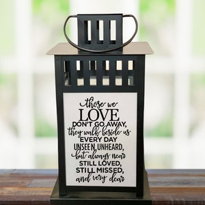 May include: Black metal lantern with a white insert featuring the text "those we LOVE DON'T GO AWAY, they walk beside us EVERY DAY UNSEEN, UNHEARD, but always near STILL LOVED, STILL MISSED, and very dear".