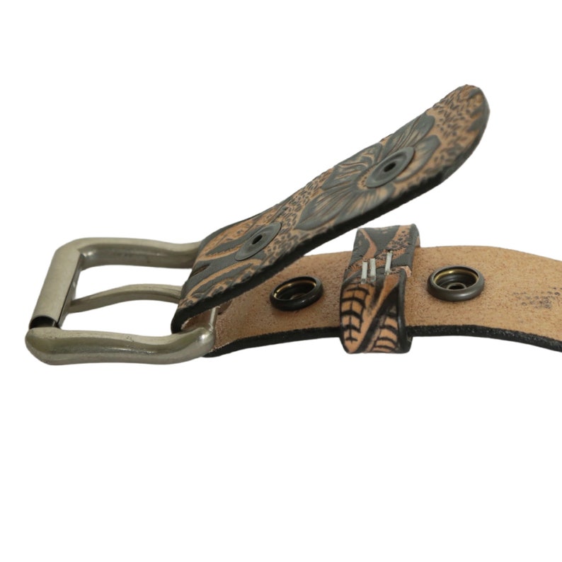 May include: A brown leather belt with a floral design and a silver buckle. The belt has multiple holes for adjusting the size.