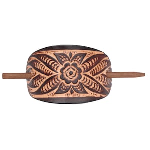 May include: A brown leather hair stick with a carved floral design. The stick is decorated with a brown and tan pattern.