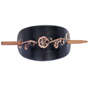 May include: Black leather hair comb with a floral design and a wooden stick. The flowers are embossed in a copper color.
