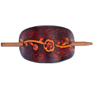 May include: A dark brown wooden hair stick with a floral design. The stick has a thin, wooden dowel that extends from the side. The floral design is in a lighter brown color and features a vine with flowers.