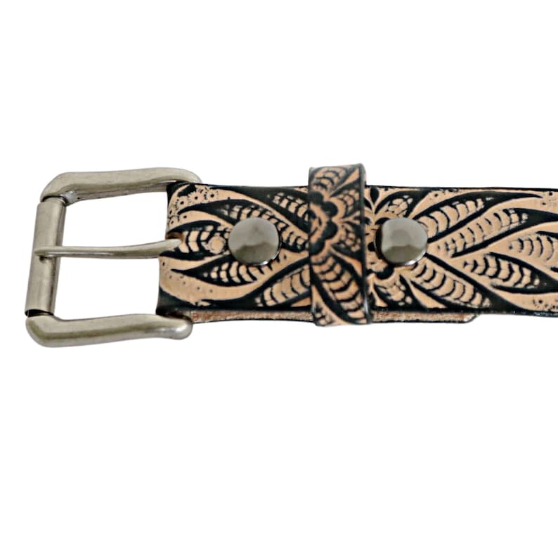 May include: A brown leather belt with a black floral design and a silver buckle. The belt has two silver rivets.