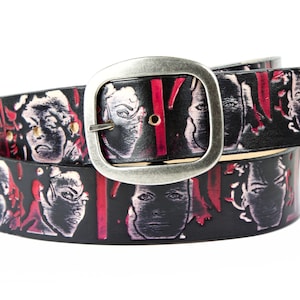 May include: A black leather belt with a silver buckle. The belt is decorated with a repeating pattern of red and white faces.