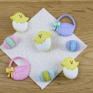 May include: A set of seven Easter-themed buttons featuring chicks, eggs, and baskets. The buttons are made of plastic and come in a variety of colours, including yellow, blue, pink, and purple.