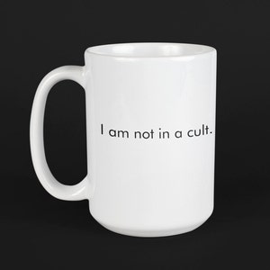 Puede incluir: Taza de café de cerámica blanca con asa negra y el texto "No estoy en un culto." impreso en la parte delantera.