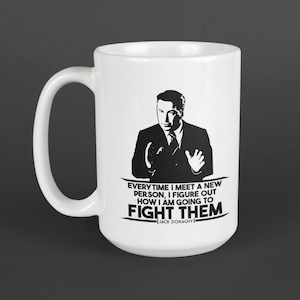 May include: White ceramic mug with a black graphic of a man in a suit and the quote, "EVERY TIME I MEET A NEW PERSON, I FIGURE OUT HOW I AM GOING TO FIGHT THEM" by Jack Donaghy.