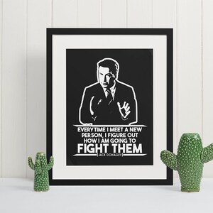 May include: Black framed print with a white graphic of a man in a suit and tie. The print includes the quote, "EVERY TIME I MEET A NEW PERSON, I FIGURE OUT HOW I AM GOING TO FIGHT THEM" by Jack Donaghy. Two green ceramic cactus figurines flank the print.
