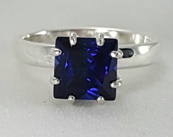 May include: A silver ring with a square-shaped blue gemstone set in a prong setting.