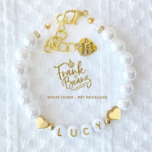 May include: White pearl necklace with a gold charm that says "Frank & Beans" and a heart charm that says "Made with Love". The necklace also has a gold heart charm and a white bead with the name "Lucy" spelled out in gold letters.