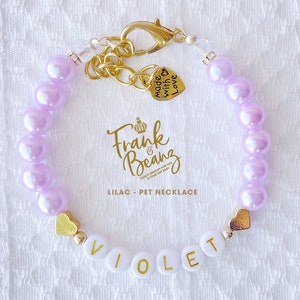 May include: Lilac pet necklace with gold heart charms and a name tag that reads "VIOLET". The necklace has a gold clasp and a charm that says "Made with Love".