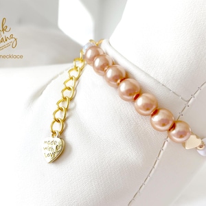 Up close white dog mannequin wearing a champagne pearl dog necklace with 14K gold heart accents with a dangling gold chain attached to a gold heart charm with the engraved words "made with love".