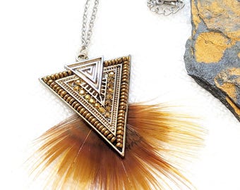 May include: A silver chain necklace with a triangular pendant. The pendant is decorated with gold beads and a geometric design. A brown feather trim hangs from the bottom of the pendant.