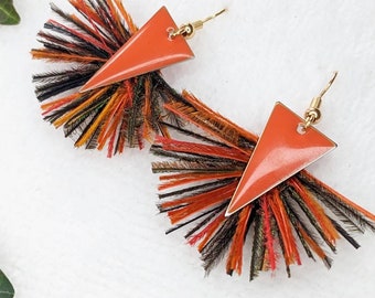 May include: A pair of orange triangle earrings with a fringe of black, orange, and brown feathers.