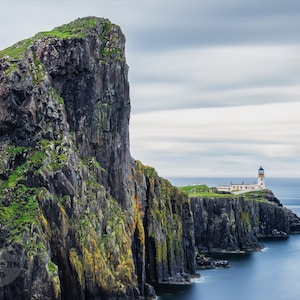 May include: A white lighthouse sits on a rocky cliff overlooking the ocean. The sky is cloudy and the water is a deep blue.