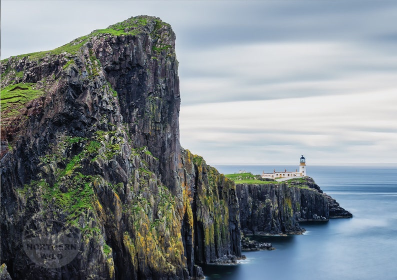 May include: A white lighthouse sits on a rocky cliff overlooking the ocean. The sky is cloudy and the water is a deep blue.