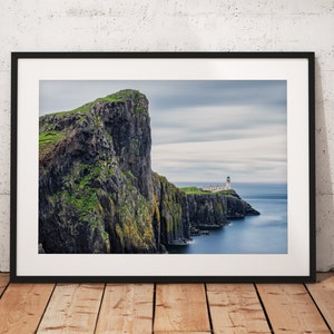 May include: A photograph of a dramatic cliff face with a lighthouse on a rocky outcropping in the distance. The sky is cloudy and the water is a deep blue.