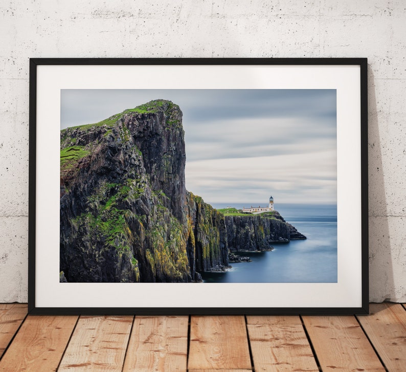 May include: A photograph of a dramatic cliff face with a lighthouse on a rocky outcropping in the distance. The sky is cloudy and the water is a deep blue.