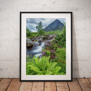 May include: A photograph of a waterfall flowing through a lush green valley with a mountain in the background. The water is flowing over rocks and the valley is filled with ferns and other plants.