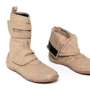May include: A pair of tan canvas high-top boots with black straps and a fold-over cuff. The boots have a rubber sole.