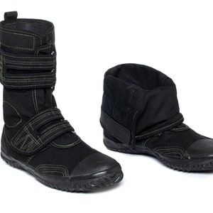 May include: Two black canvas boots with rubber soles. One boot is high-top with adjustable straps and green stitching. The other boot is a low-top style with a folded-down cuff and a single strap.