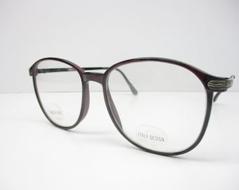 May include: A pair of brown oval-shaped spectacles with a metal bridge and a silver accent on the temple. The glasses have clear lenses and say "ITALY DESIGN" on the right lens.