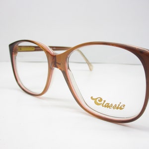 May include: Brown plastic framed spectacles with a gold "Classic" logo on the right lens.