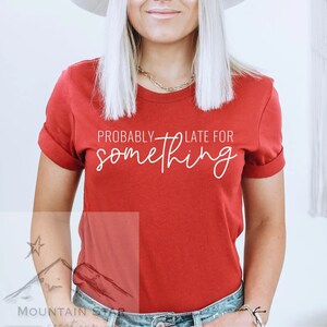 May include: Red short-sleeved t-shirt with white text that reads "Probably Late For Something".