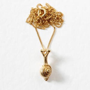 May include: A gold chain necklace with a snail pendant. The snail is detailed with a textured shell and a long, slender body.