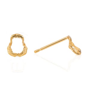 May include: A pair of gold shark tooth earrings. The earrings are made of a detailed, realistic shark tooth design. The earrings are shown on a white background.