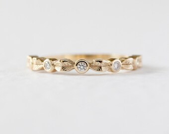 May include: A gold ring with a leaf design and small, round diamonds. The ring has a delicate, nature-inspired pattern with alternating leaves and gemstones. The ring is set against a white background.