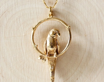 May include: A gold necklace with a pendant featuring a parrot perched on a branch. The parrot is detailed with a textured body and a pink eye.