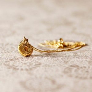 May include: A gold necklace with a round pendant that resembles a flower. The pendant has a textured, circular design.
